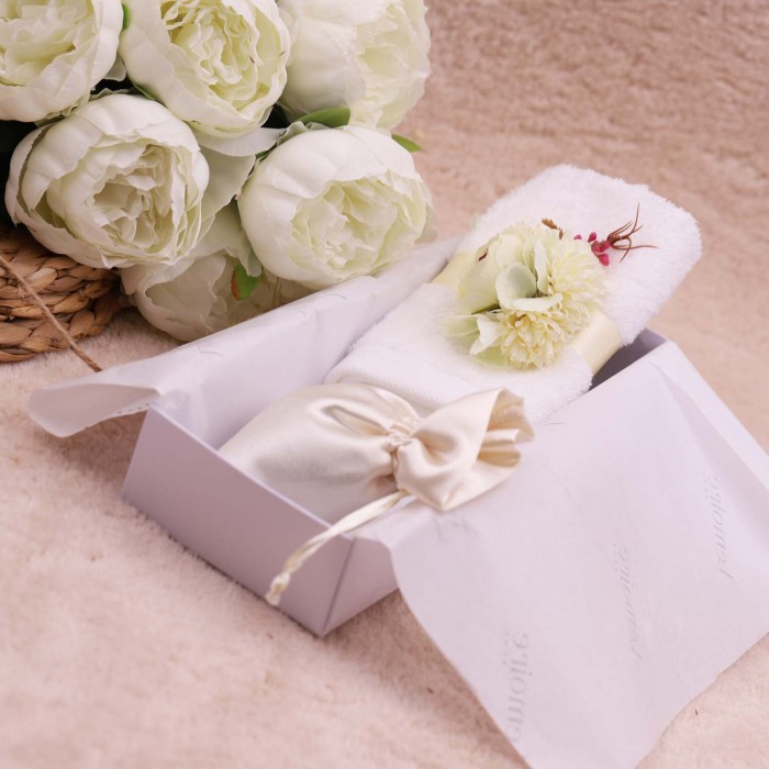Asciugamano bianco chiuso da un giro di nastro e un bouquet di peonie avorio